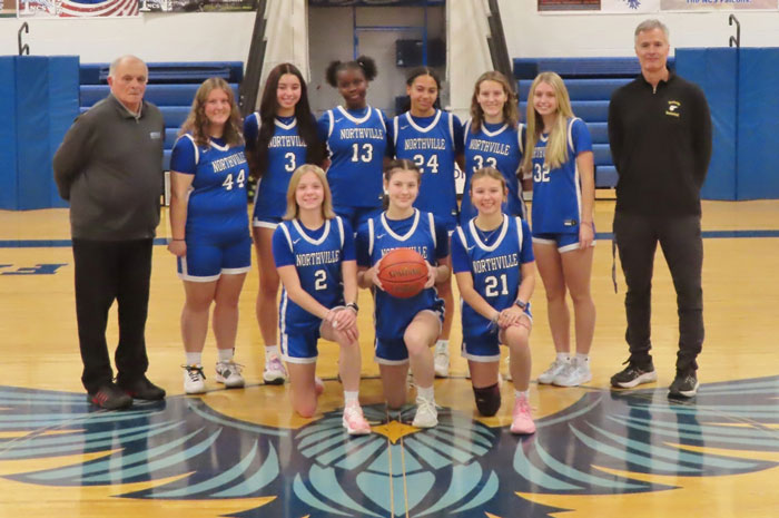 High school basketball team posing on the court with two coaches in an indoor gym.