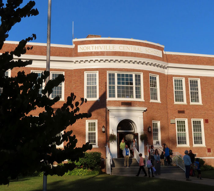 Northville Central School entrance, with people entering and leaving, under a clear sky.