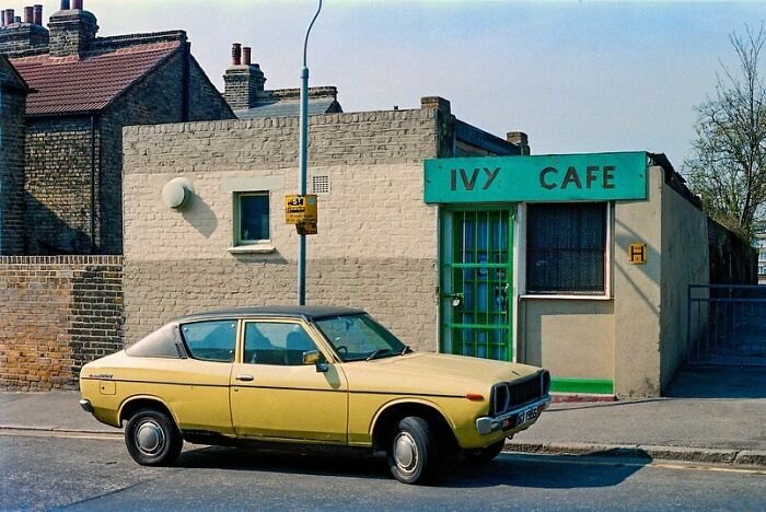 Vintage yellow car parked in front of the Ivy Cafe, with nostalgic brick buildings in the background.