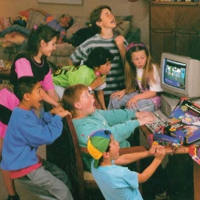 Kids in colorful outfits gathered around an old computer, showcasing a funny throwback moment.