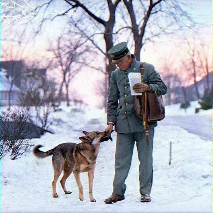 Mailman in winter uniform interacting with a dog on a snowy path, illustrating historical daily life moments.