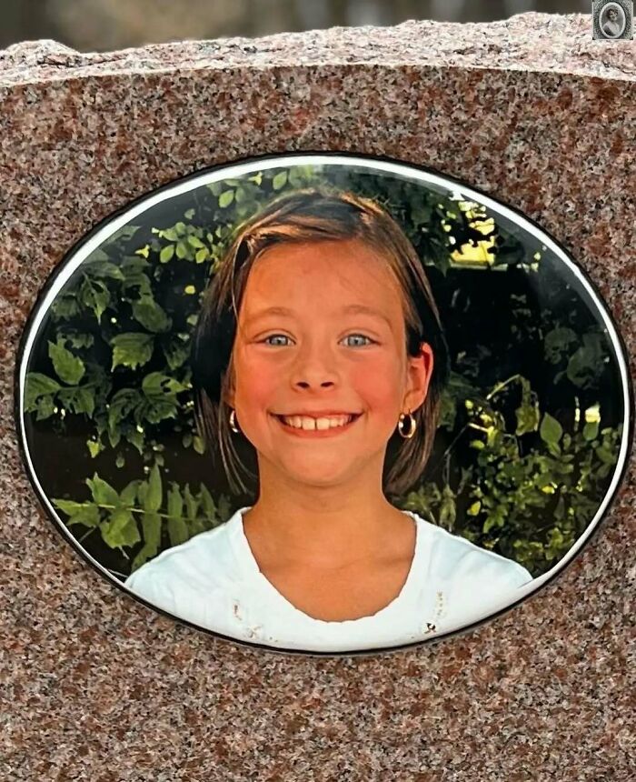 Portrait of a smiling girl on a lovely headstone, surrounded by foliage.