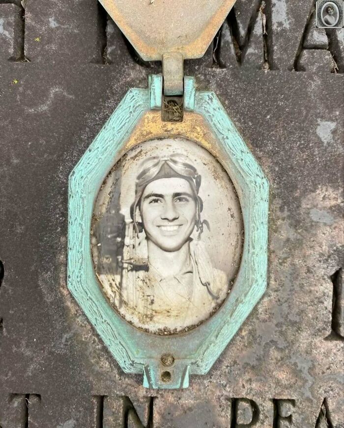 Old black-and-white headstone portrait of a smiling man in a pilot's outfit, framed by a weathered metal oval.