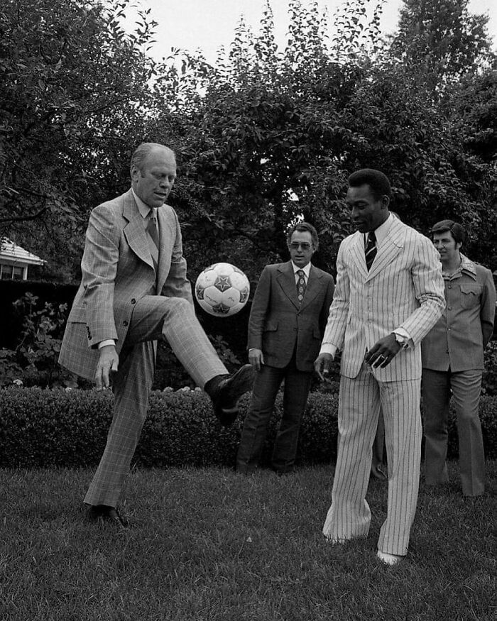 A man in a suit playing soccer with another in a striped suit, showcasing historical interactions with famous athletes.