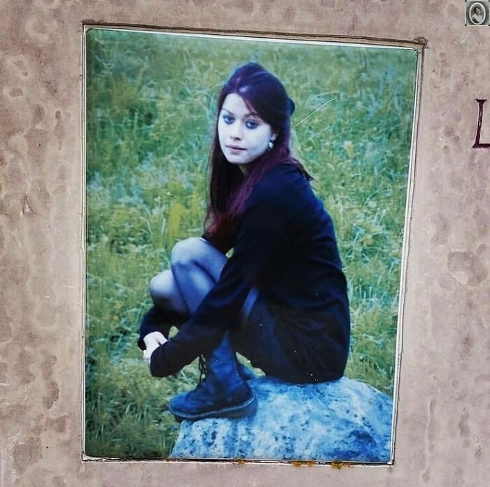 Woman sitting on a rock in a headstone portrait, wearing a black outfit and boots.