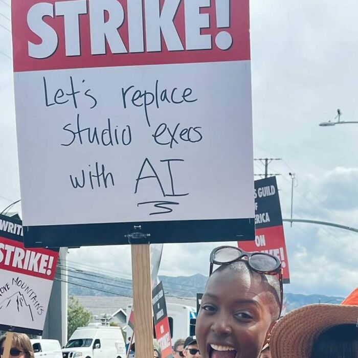Person holding a sign reading "Let's replace studio execs with AI" during a strike protest.