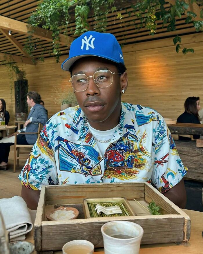 Person in colorful shirt and blue cap enjoying a wooden tray meal, embodying classy celeb style.