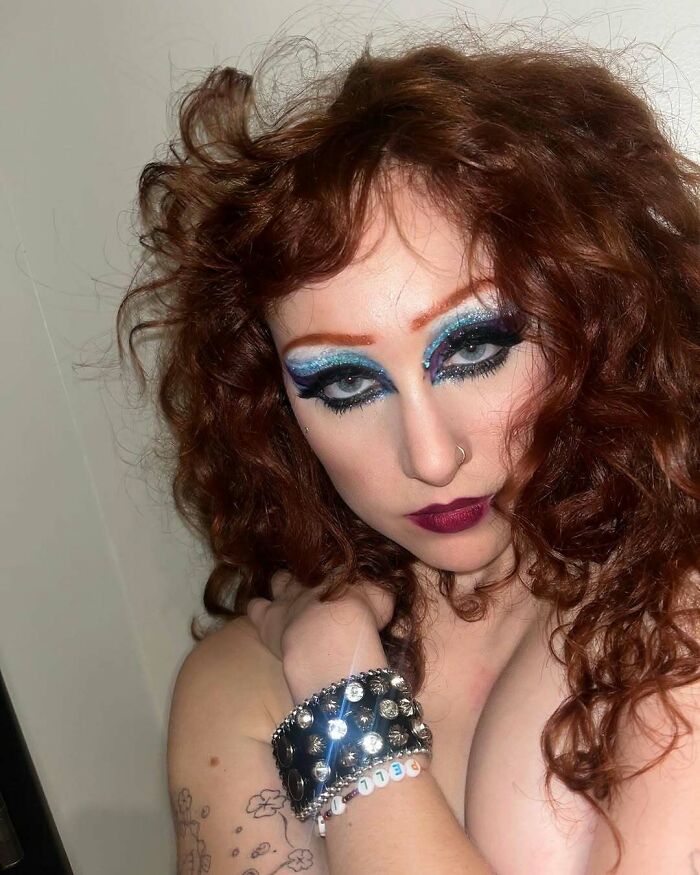 Celeb with curly red hair and bold makeup, wearing a studded bracelet, showcasing a classy clap back style.