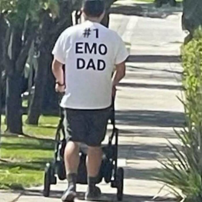 Man walking with a stroller, wearing a white t-shirt that says "#1 Emo Dad," showing off chaotic t-shirt truth.