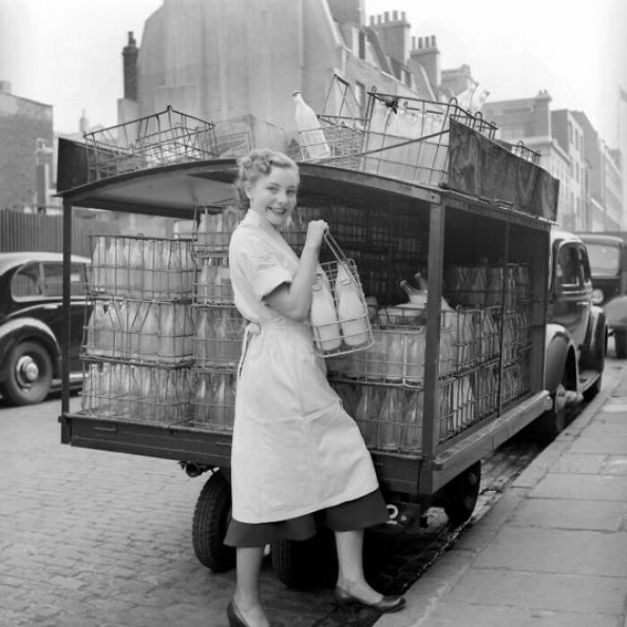Vintage image of a milk delivery woman in the 1940s, holding milk bottles near a cart loaded with crates.