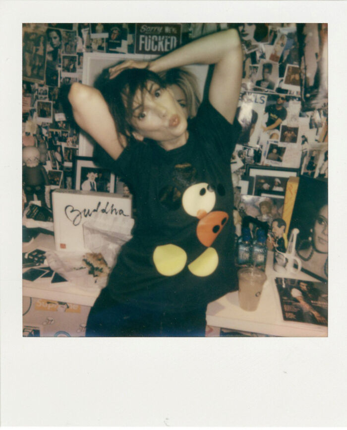 A person posing playfully in a room filled with historical photos and eclectic decorations.