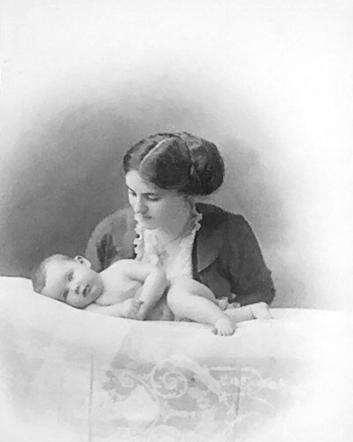 A historical photo of a woman from the past lovingly holding a baby in a serene setting.