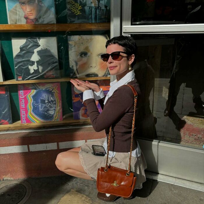 Woman showcasing record shop display with albums, sunglasses, brown sweater, and handbag; example of petty celebrity moments.