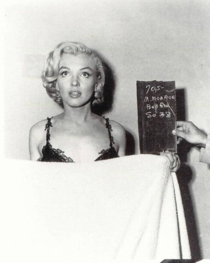 Black-and-white historical photo, woman with curly hair holding a slate, wrapped in a towel.