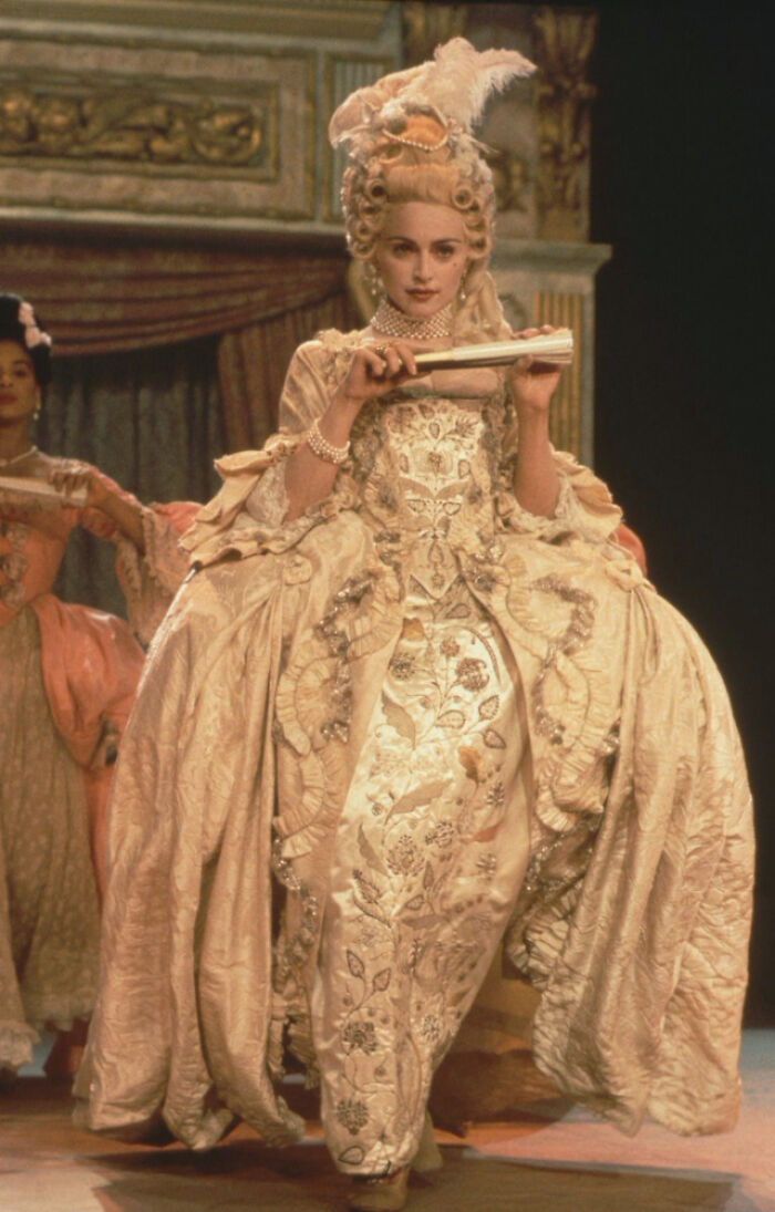 Historical photo of a woman in ornate 18th-century costume holding a fan, offering a glimpse into the past.