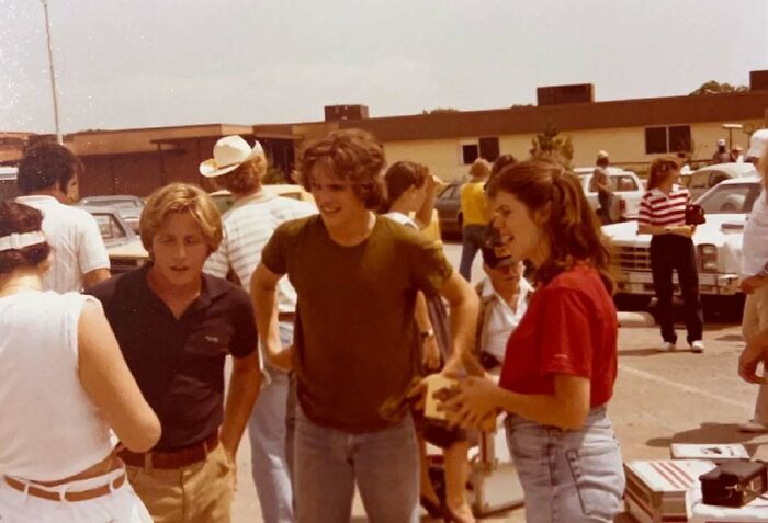 Young people in casual attire conversing outdoors, offering a glimpse of historical fashion and social interaction.