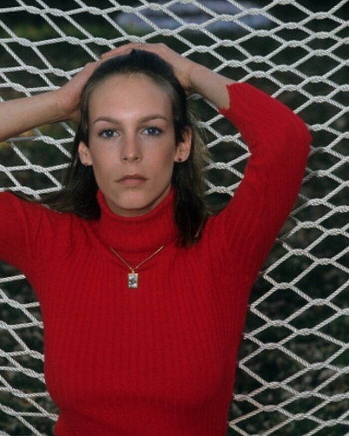 Person in a red turtleneck with hands on head, standing against a net backdrop, offering a glimpse into the historical past.