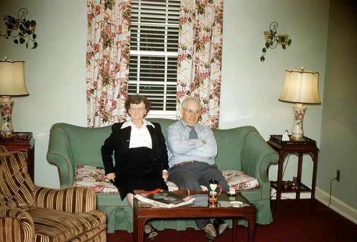 Elderly couple sitting on a vintage couch in a living room, offering a historical look into the past with classic decor.