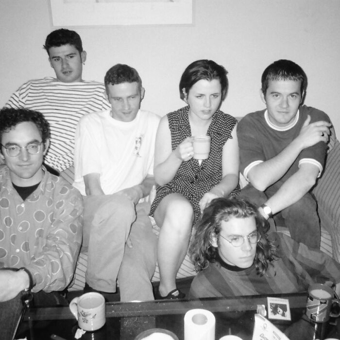 Black and white historical photo of a group sitting on a sofa, capturing a moment from the past.
