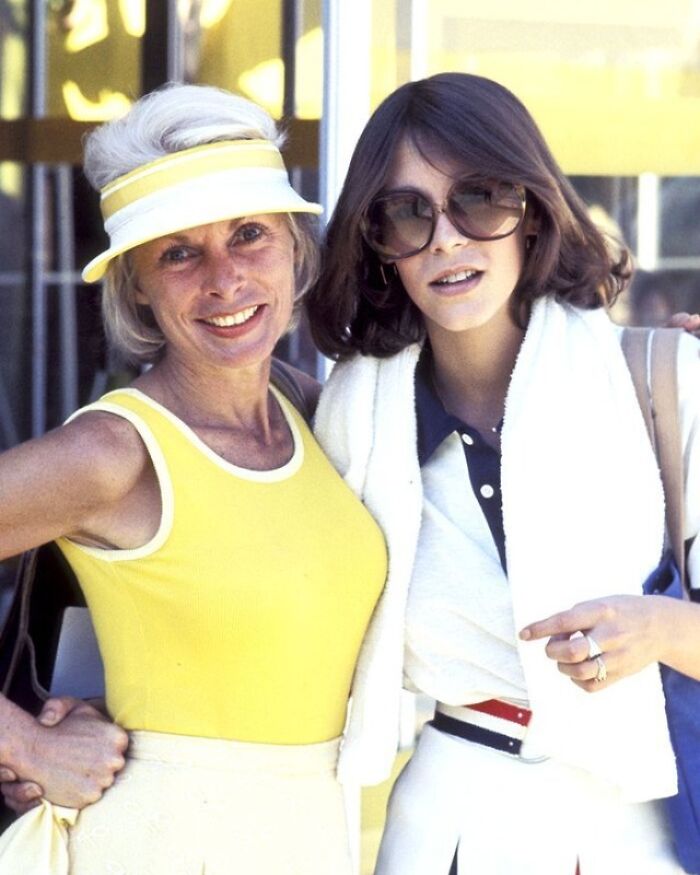 Two women in 1970s fashion, one in yellow, embracing and smiling outdoors, offering a fascinating look into the past.