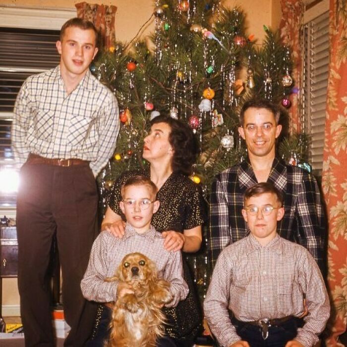 Family posing with a decorated Christmas tree, capturing a historical moment from the past.