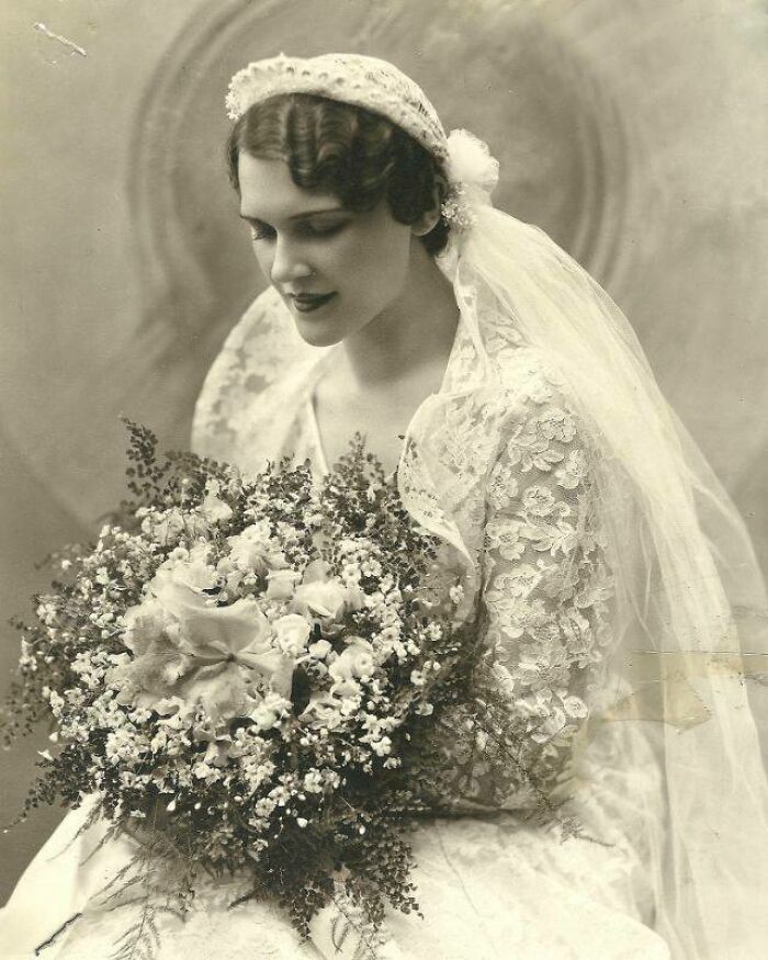 Historical photo of a bride in lace dress holding a large bouquet, capturing a vintage moment from the past.