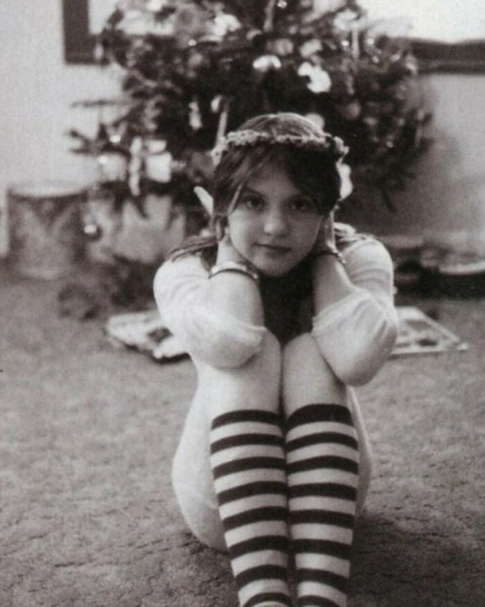 Young girl with striped socks sitting by a historical Christmas tree, offering a glimpse into the past.