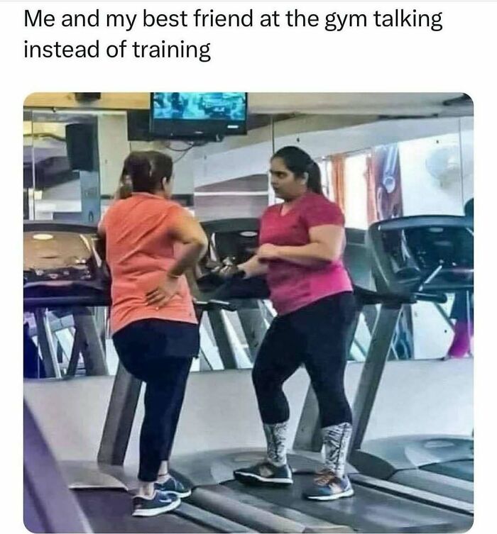 Two women chatting on treadmills in a gym, enjoying a lighthearted moment together.