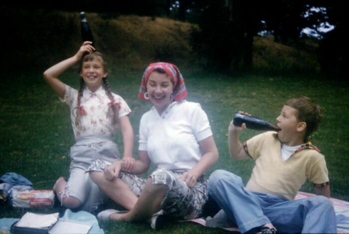 Children enjoying a picnic in the past, with soda bottles and playful expressions, on a grassy field.