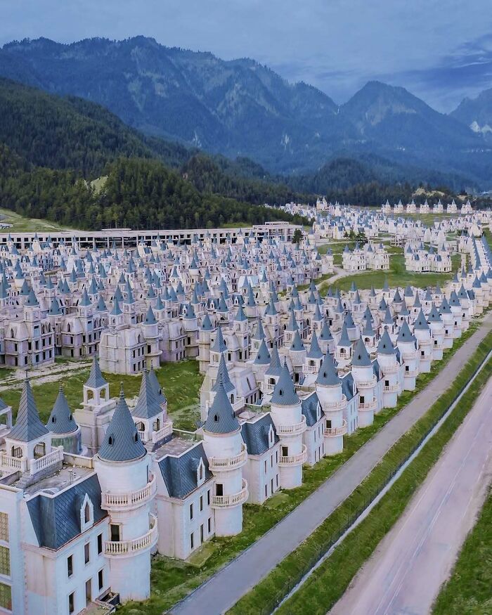 Aerial view of numerous identical castle-like homes lined up against a mountainous backdrop.