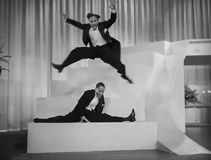 Two performers in tuxedos dancing energetically on stage, offering a fascinating glimpse into historical performances.