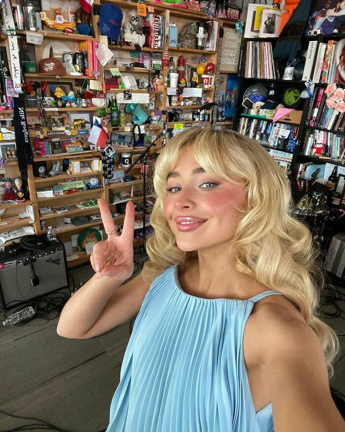 Person in a blue dress posing with a peace sign in a room full of colorful items.