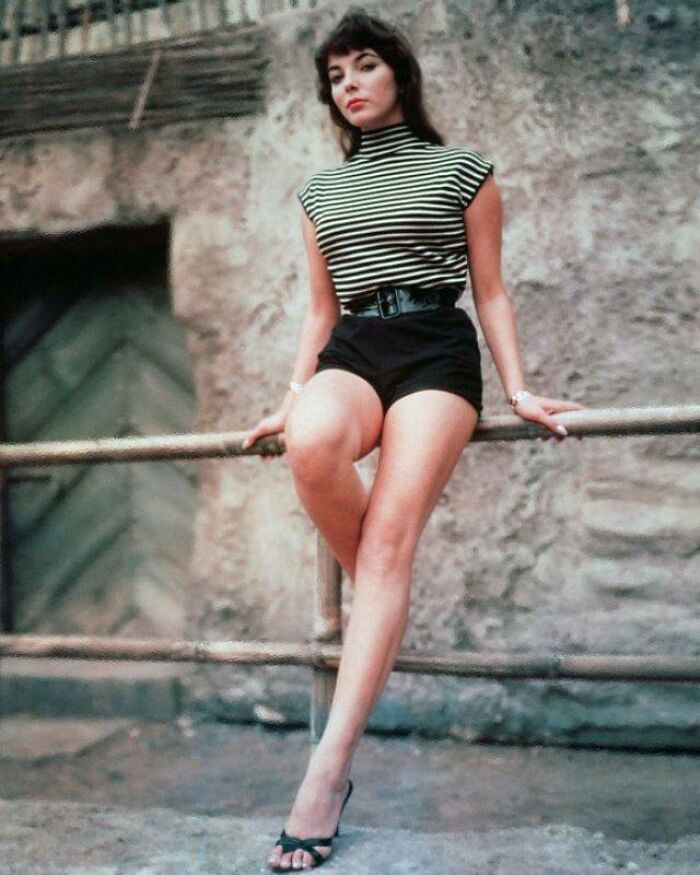 Woman in striped top and shorts, sitting on a railing, offering a glimpse into historical fashion.