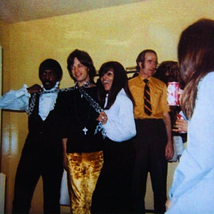 Group of people in 1970s attire enjoying a social event, capturing a fascinating historical moment.