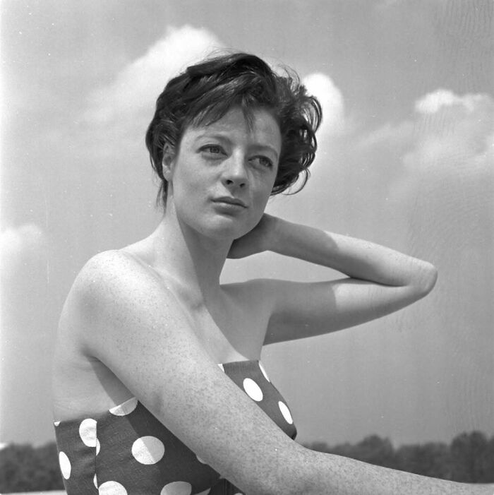 "Vintage photograph of a woman in a polka-dot dress, looking into the distance against a cloudy sky backdrop, symbolizing the past."