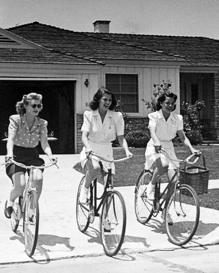 Women riding bicycles in vintage attire, capturing a historical moment from the past.