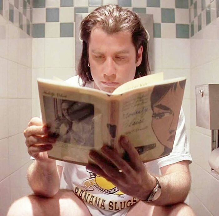 Person reading a book on a toilet, representing a humorous moment from the ‘90s.