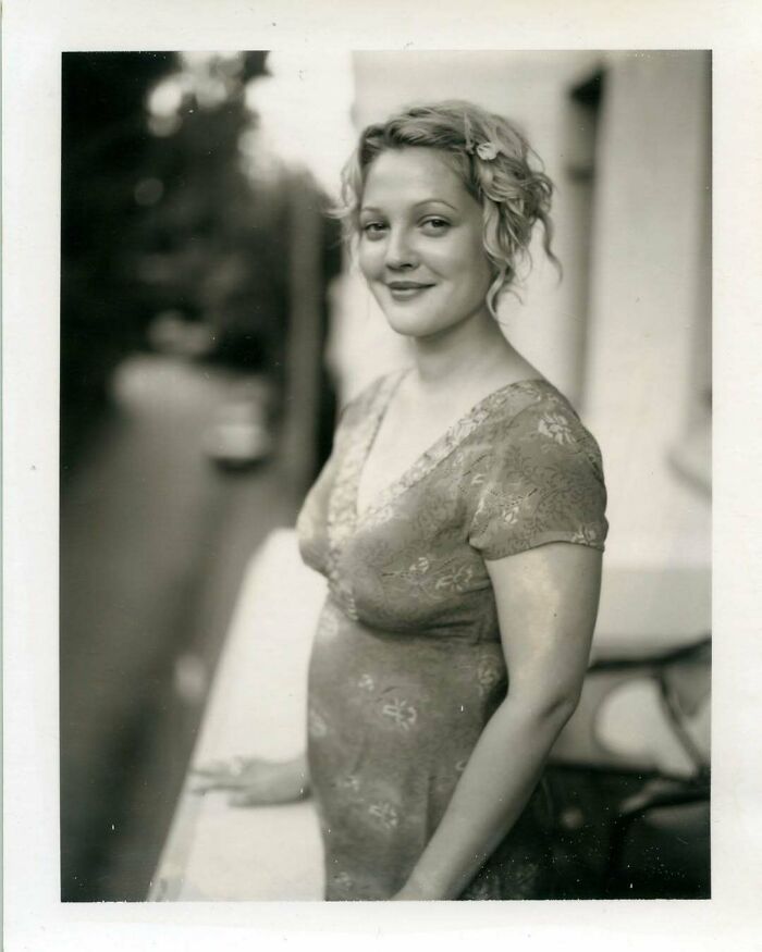Woman in a vintage dress smiling on a balcony, black and white photo showcasing historical fashion.