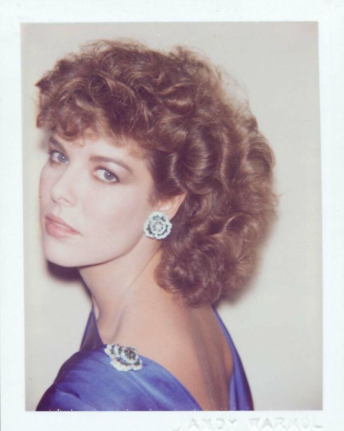 Young woman in a blue dress with floral earrings, captured in a vintage photograph for a historical collection.