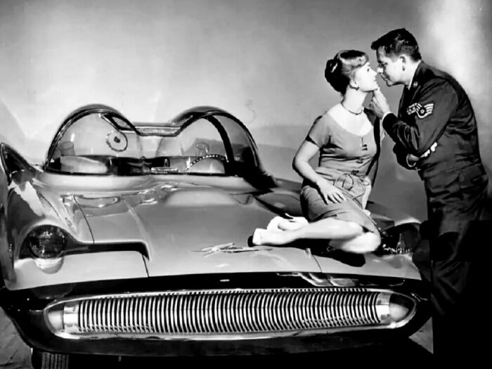 A couple shares a moment on a vintage car, evoking a historical glimpse into the past.