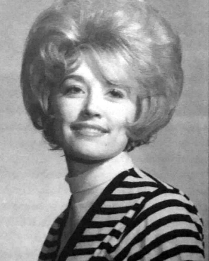 A black and white historical photo of a woman with voluminous hair wearing a striped outfit.