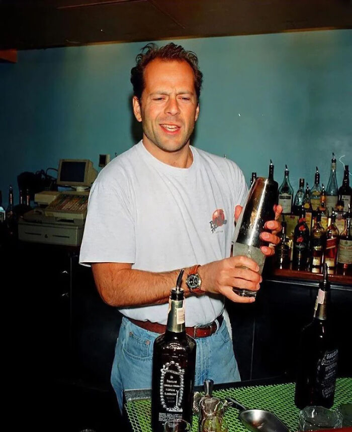 Man in a bar setting, wearing a white shirt, holding a cocktail shaker, offering a fascinating look into the past.