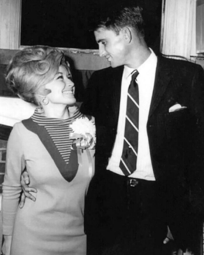 A couple smiling at each other in a historical photo, showcasing vintage fashion and hairstyles.