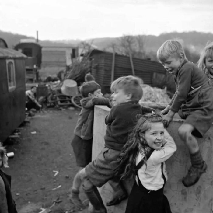 Children playing around a wooden structure in a historical photo, capturing a moment from the past.