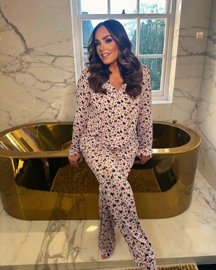 Celebrity posing in a luxurious bathroom in pink patterned loungewear with a gold bathtub.