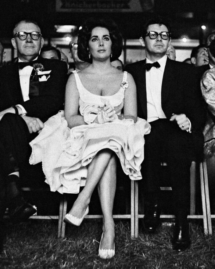 Elegant woman in a vintage dress sitting between two men at an event, offering a glimpse into the past.