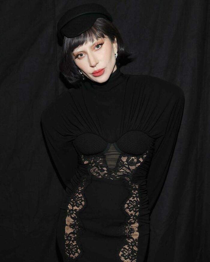 A woman in an elegant black lace dress and hat poses against a dark backdrop, relating to wasteful celebrity actions.