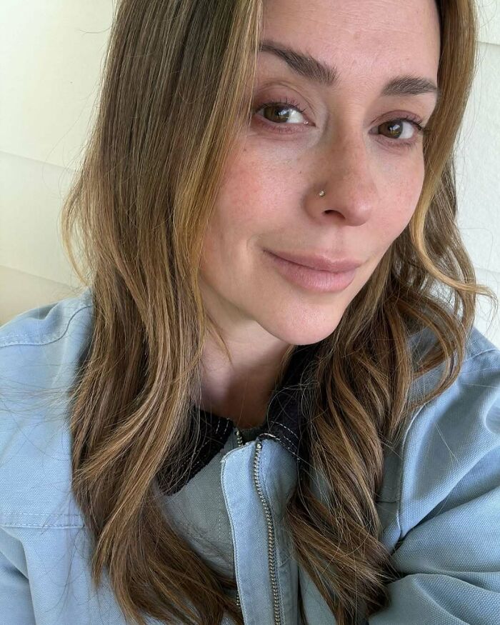 Celebrity with long hair, wearing light blue top, smiling subtly.