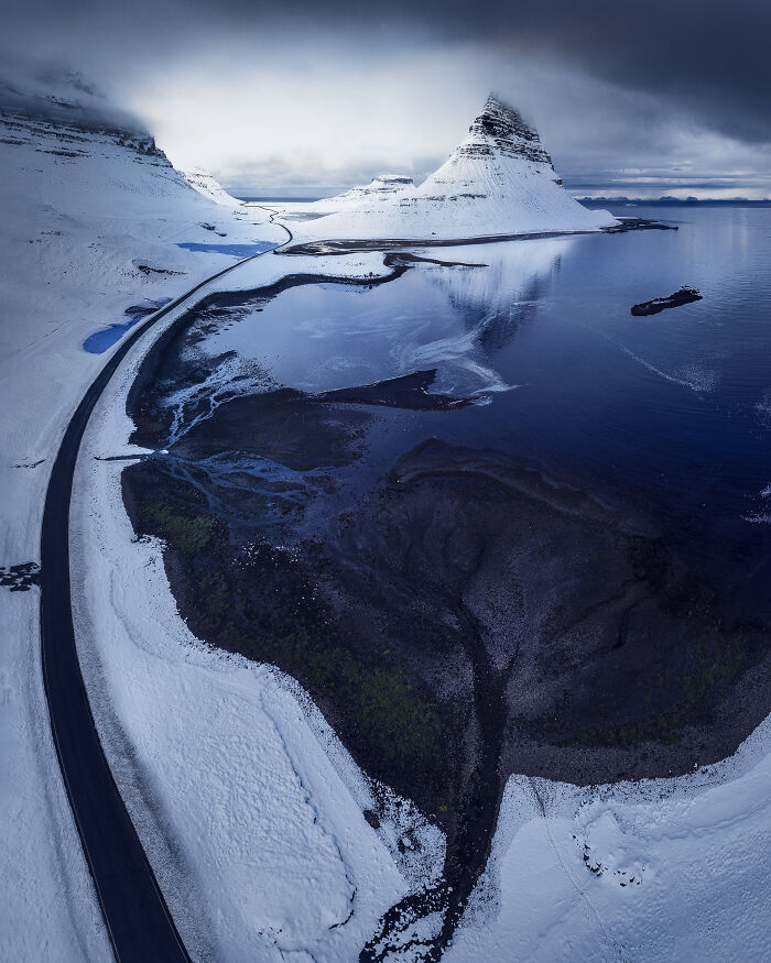 Stunning landscape with snow-covered mountain and winding road by the sea, captured by a photographer.
