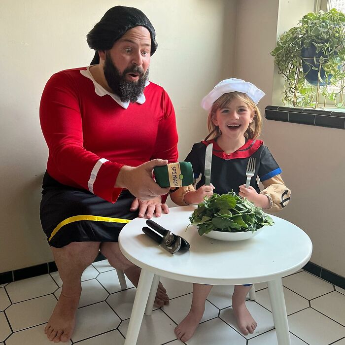Dad and daughter in costumes at a table with spinach, creating a funny and adorable scene.
